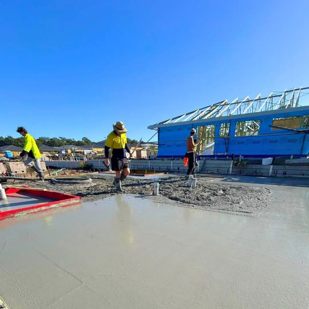 Crew finishing a fresh slab beside a new house frame